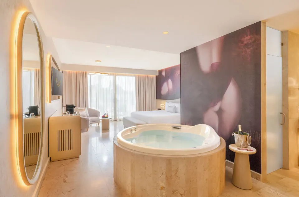 In-room round Jacuzzi and king bed in a Beloved Tropical View Jacuzzi Suite at Desire Riviera Maya Resort.