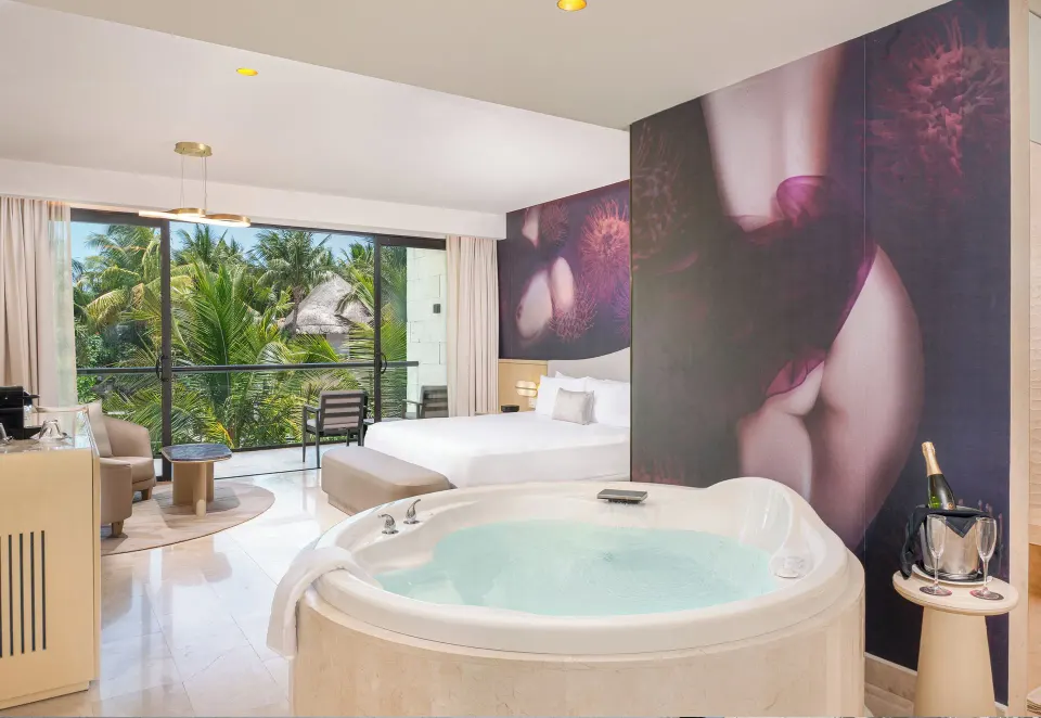 Jacuzzi, king bed, and tropical balcony view in a suite at Desire Riviera Maya Resort.