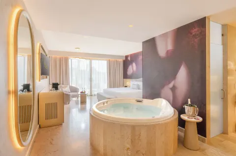 Beloved Tropical-View Jacuzzi Suite with indoor tub, king bed, and illuminated mirror at Desire Riviera Maya Resort.