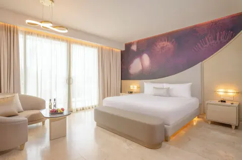 Beloved Tropical-View Jacuzzi Suite king bed with lounge seating and sheer curtains at Desire Riviera Maya Resort.