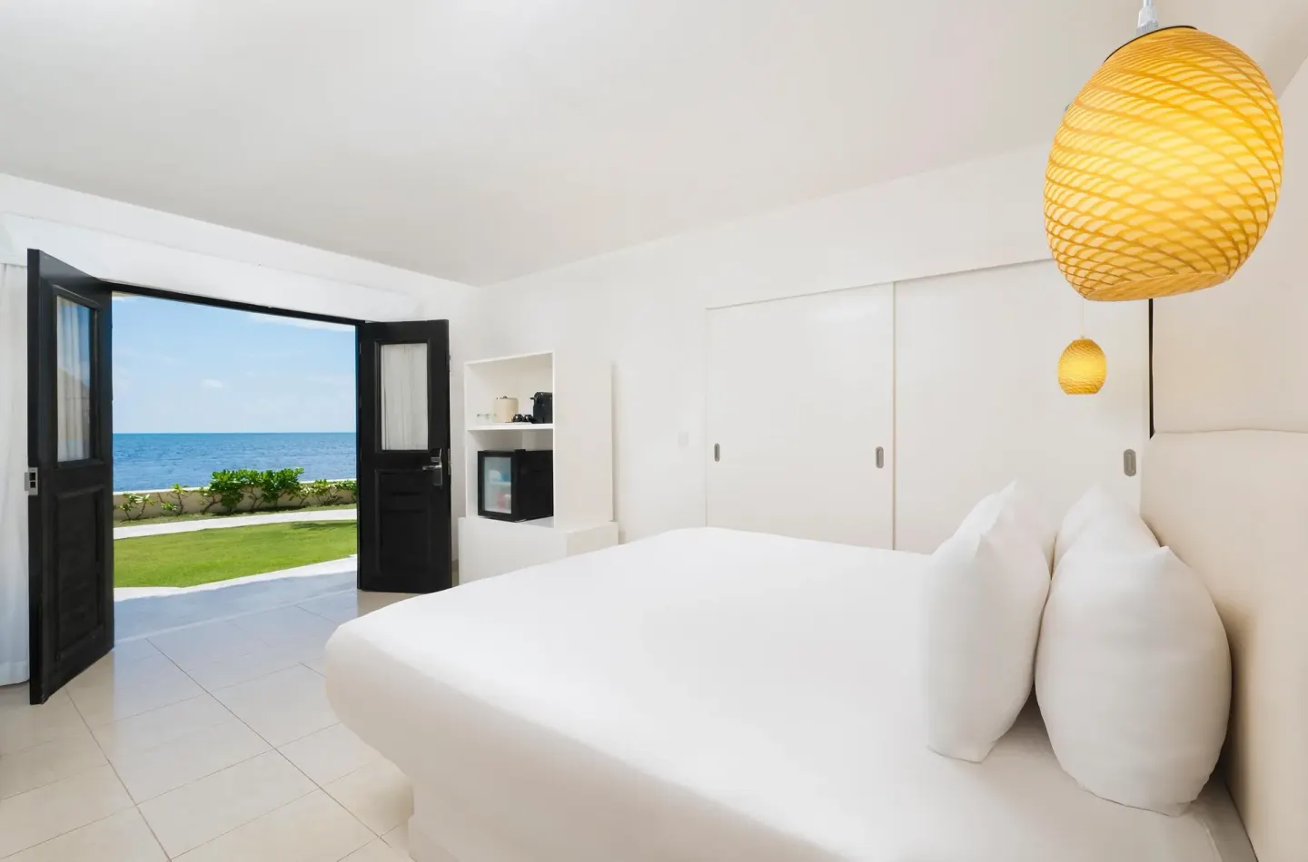 Deluxe Ocean View Room with white bed and open doors to the sea at Desire Riviera Maya Resort.