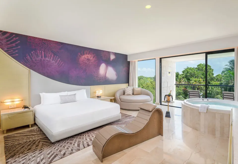 Jacuzzi suite with king bed, round tub, balcony, and tropical greenery at Desire Riviera Maya Resort.