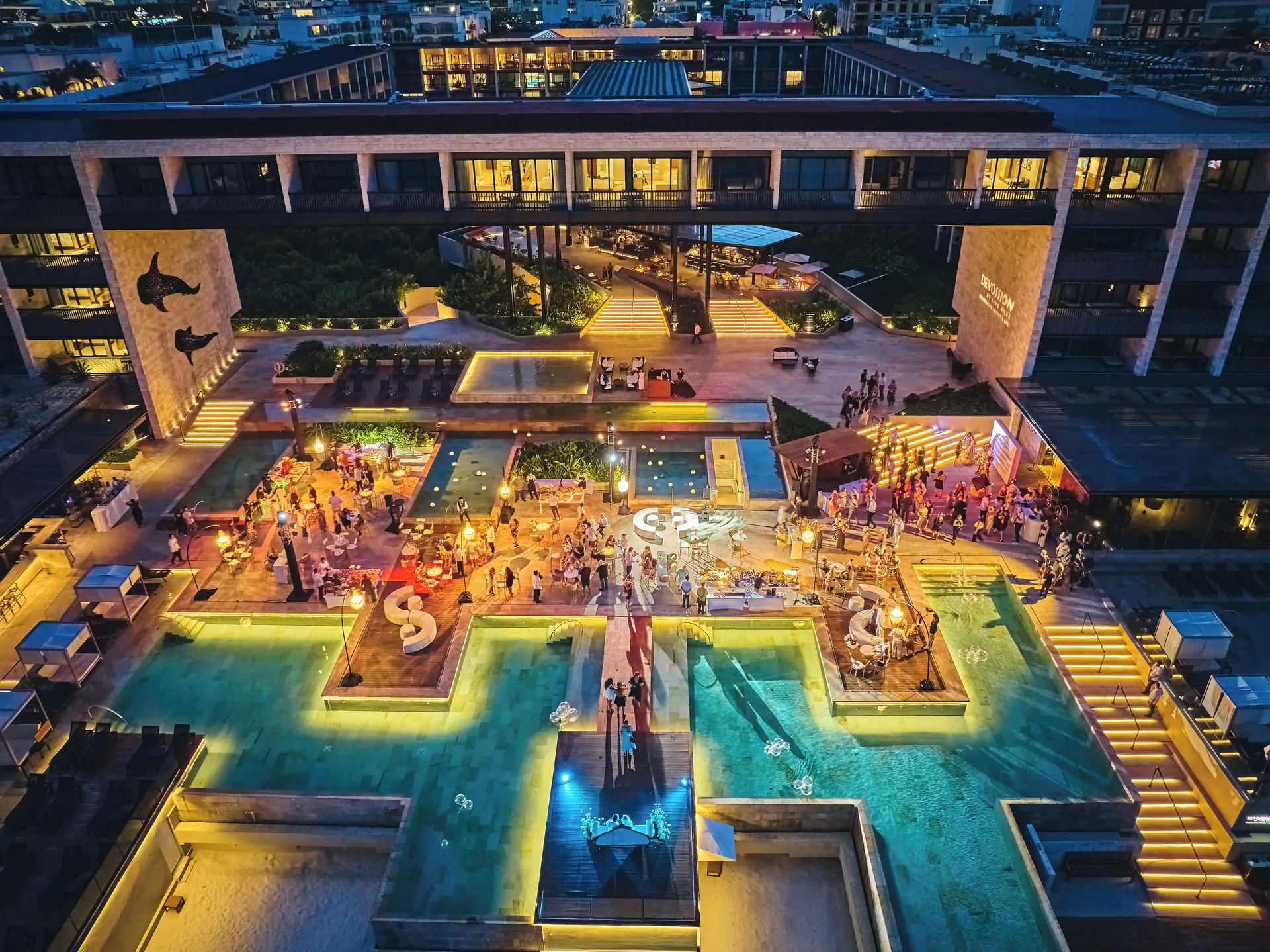 Illuminated pool deck and evening gathering at Devossion By Live Aqua Playa del Carmen.