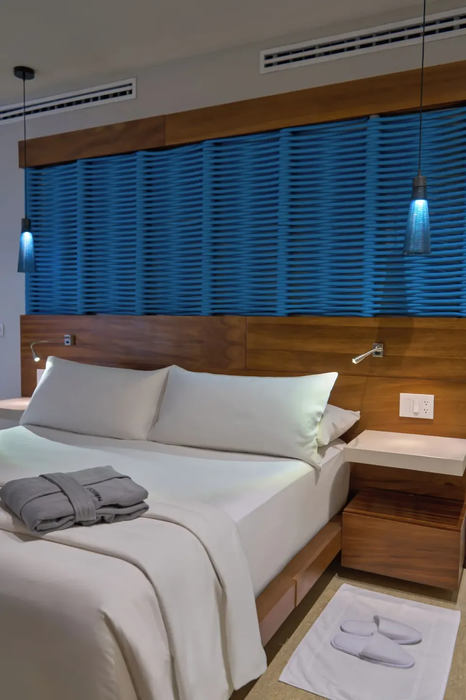 King bed detail with blue headboard accent at Devossion By Live Aqua Playa del Carmen.