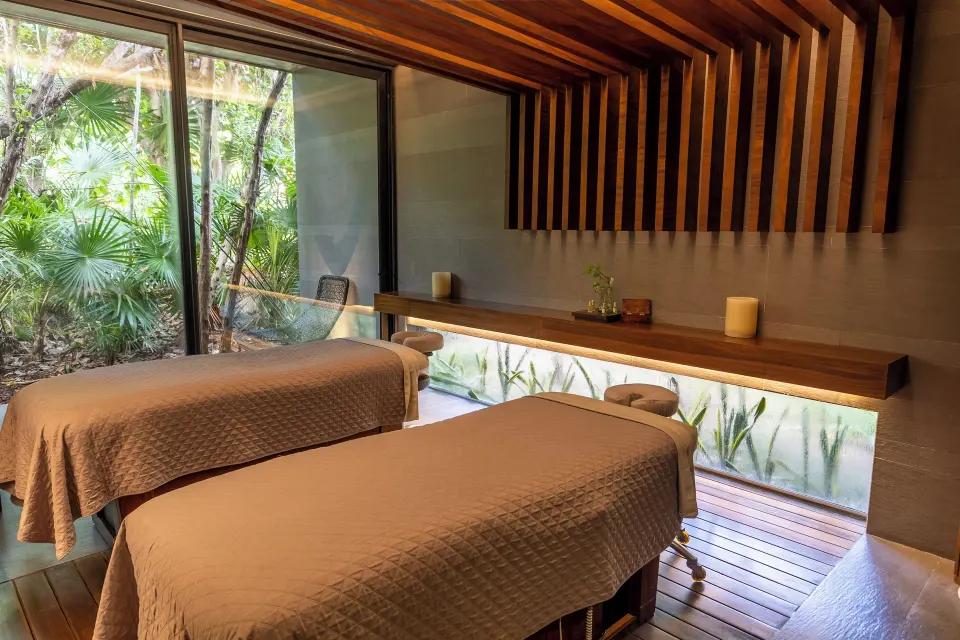 Two spa treatment tables beside jungle-facing windows at Devossion By Live Aqua Playa del Carmen.