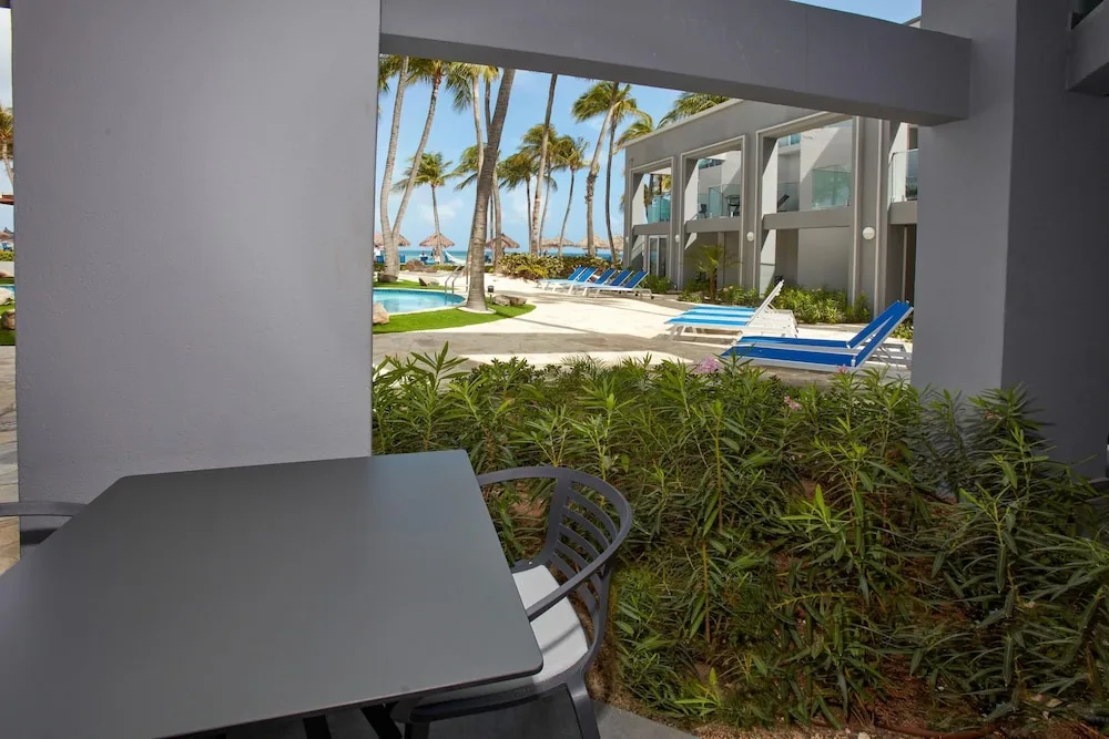 Patio seating facing pool loungers and palms at Divi Aruba Phoenix Beach Resort.