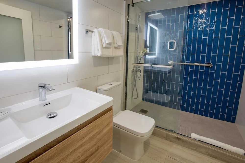 Guest bathroom with vanity, towels, and blue tile shower at Divi Aruba Phoenix Beach Resort.