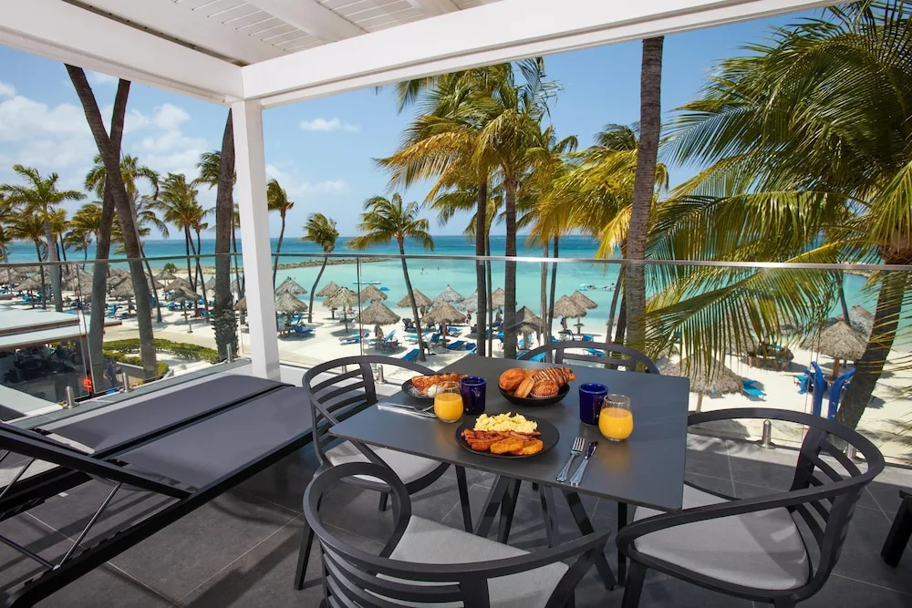 Oceanfront balcony breakfast with beach and palm views at Divi Aruba Phoenix Beach Resort.