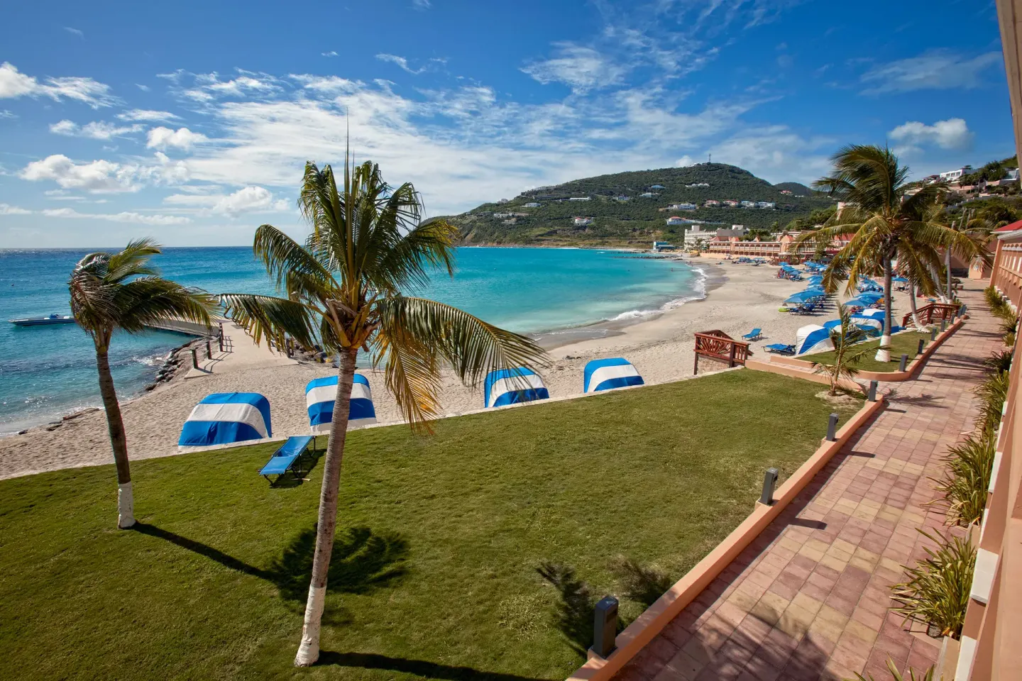 Beachfront lawn, palm trees, umbrellas, and bay at Divi Little Bay Beach Resort.