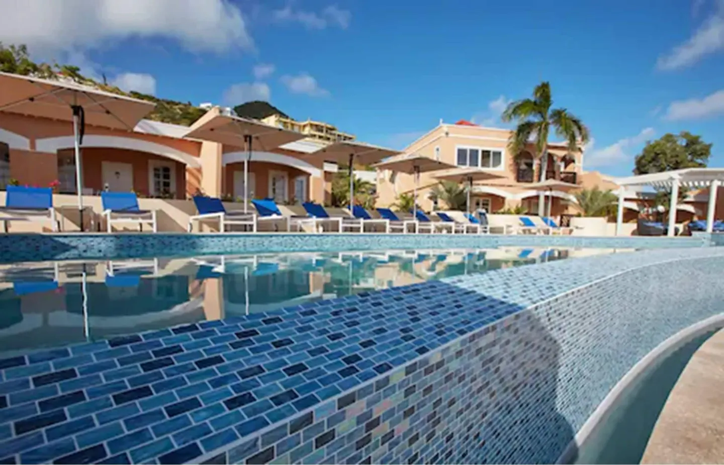 Mosaic-tiled pool edge with loungers and umbrellas at Divi Little Bay Beach Resort.