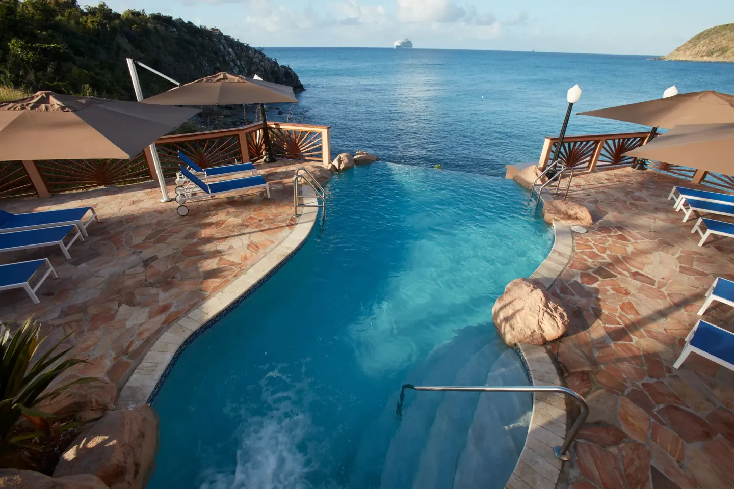 Oceanfront pool with blue loungers and umbrellas at Divi Little Bay Beach Resort.