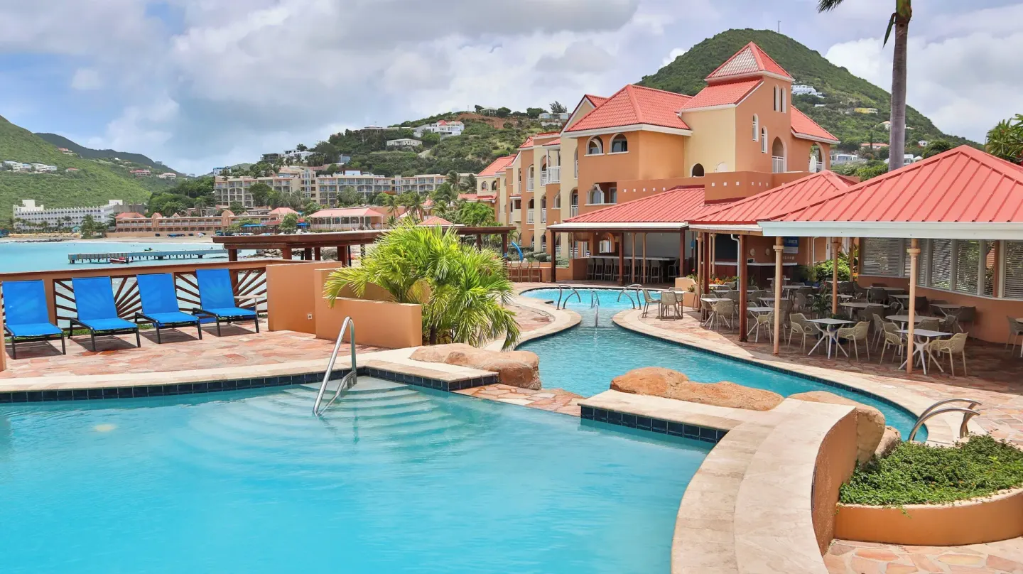 Pool terrace with red-roof buildings and bay view at Divi Little Bay Beach Resort.