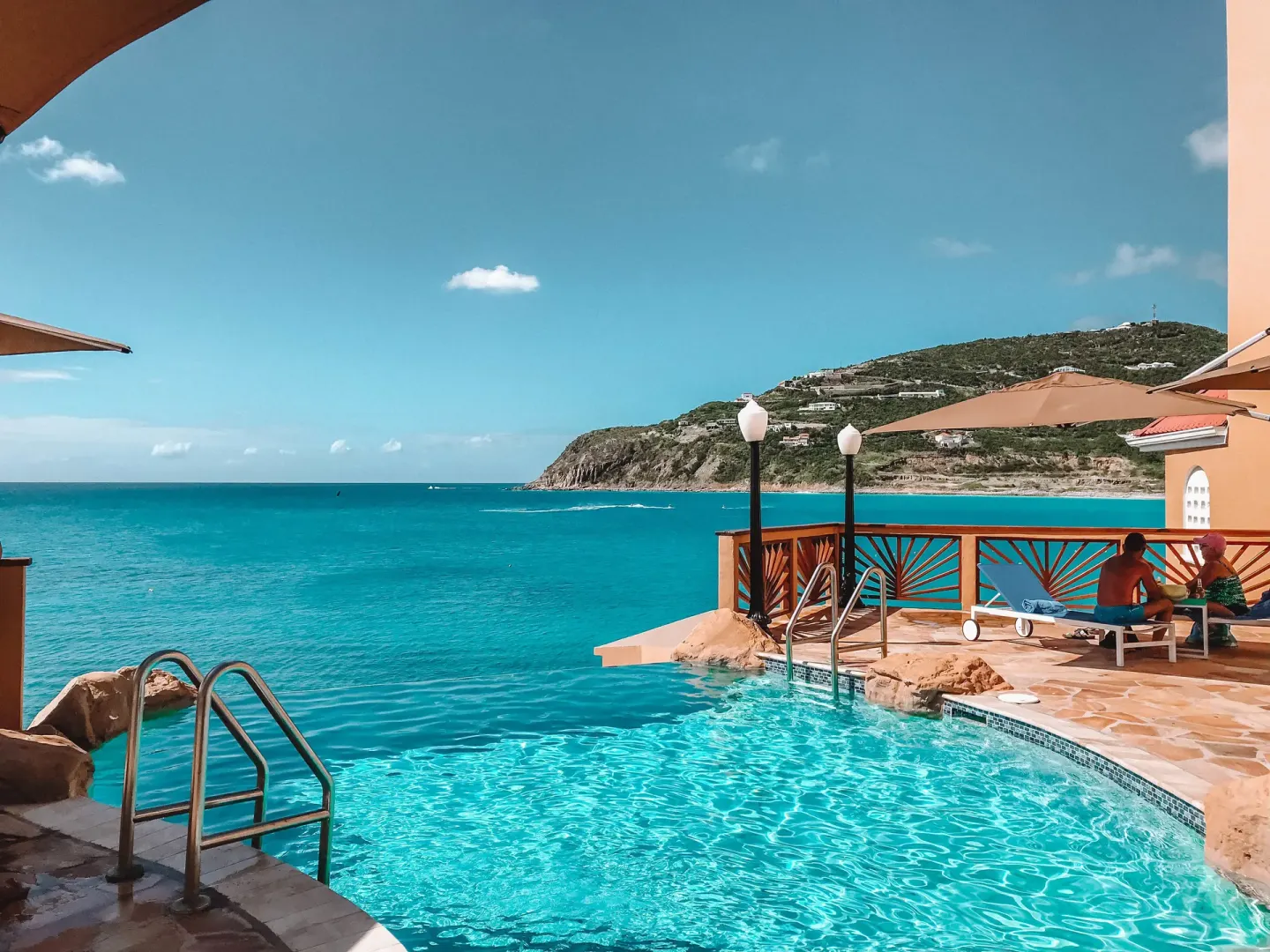 Pool steps and loungers face the turquoise bay at Divi Little Bay Beach Resort.