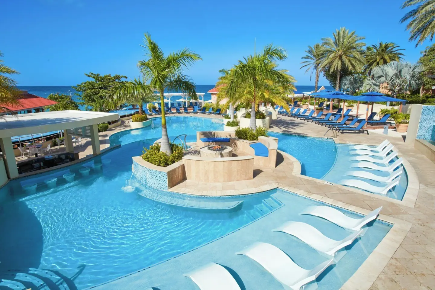 Pool with in-water loungers and palm trees at Divi Little Bay Beach Resort.