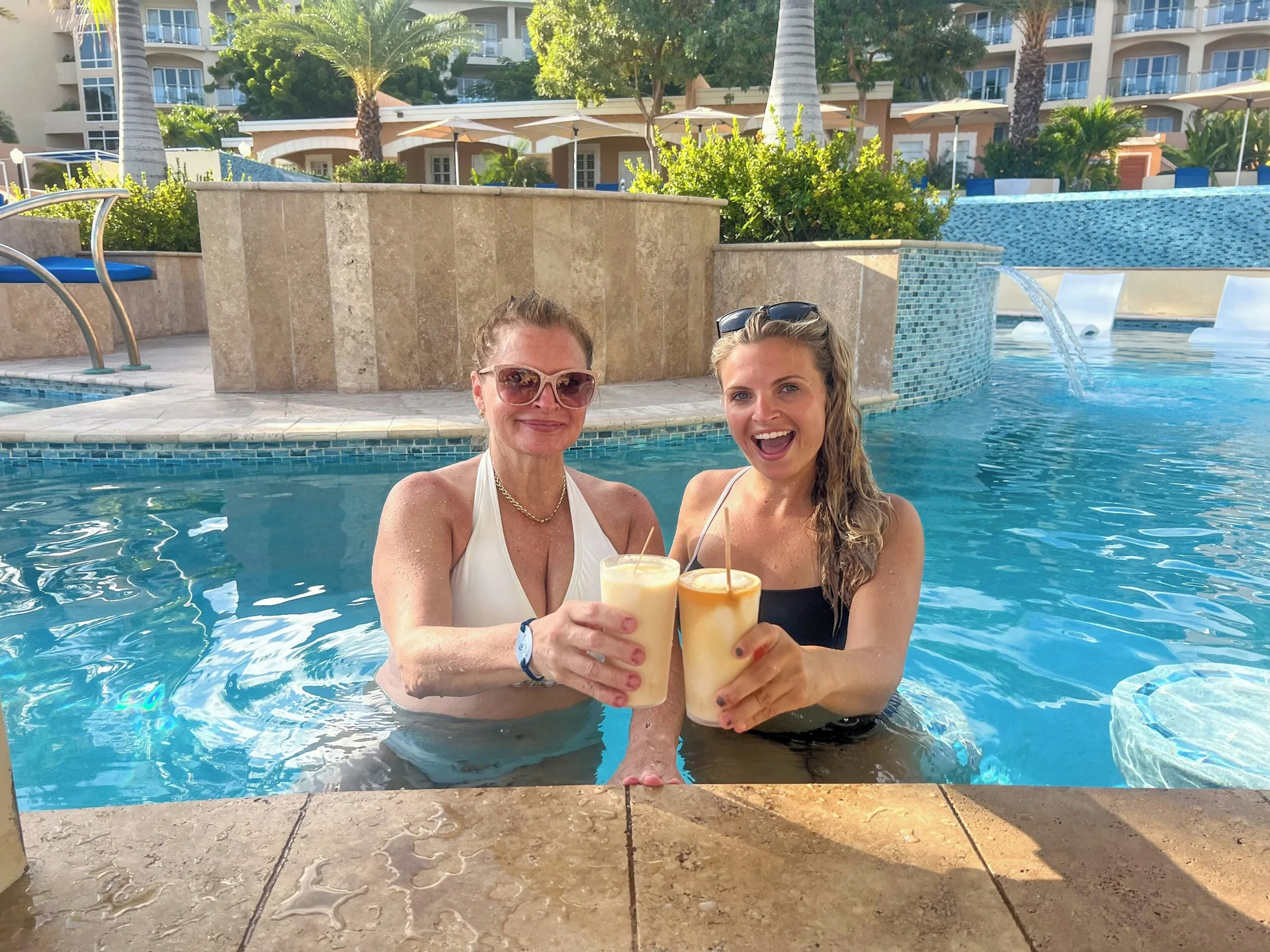Two guests toast frozen drinks in the pool at Divi Little Bay Beach Resort.