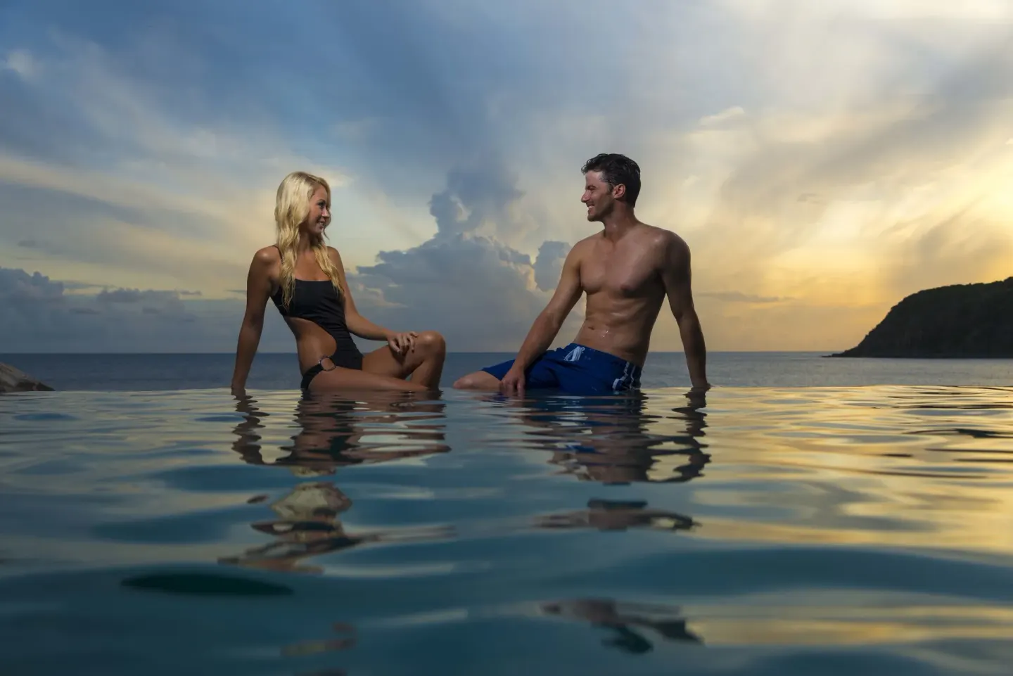 Two guests sit in an infinity pool at sunset at Divi Little Bay Beach Resort.