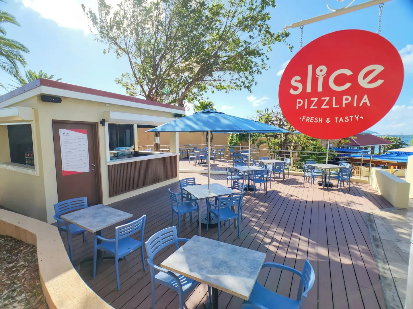 Slice Pizzeria patio with blue chairs and a red sign at Divi Little Bay Beach Resort.
