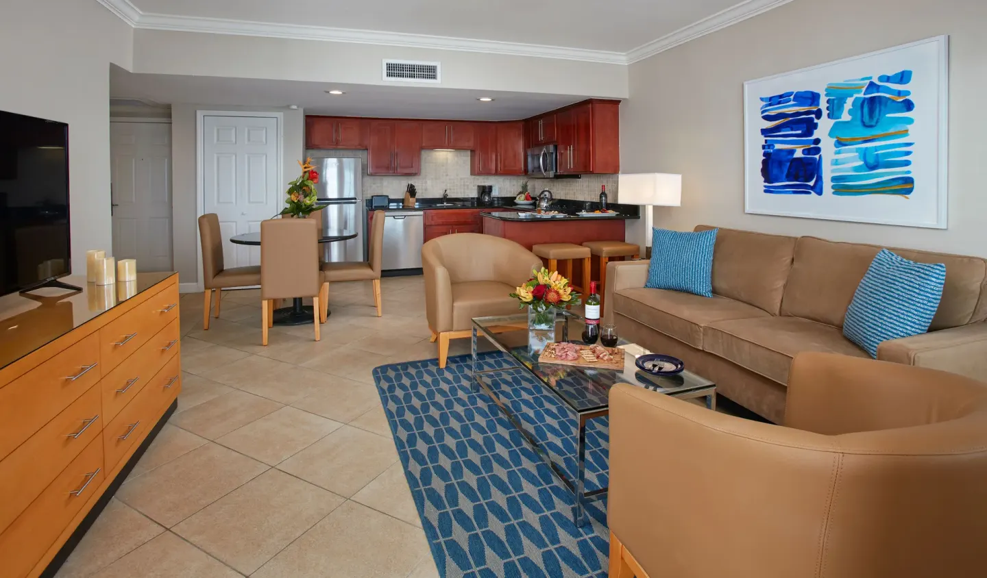 One-bedroom suite lounge with sofa, TV, dining nook, and kitchen at Divi Little Bay Beach Resort.