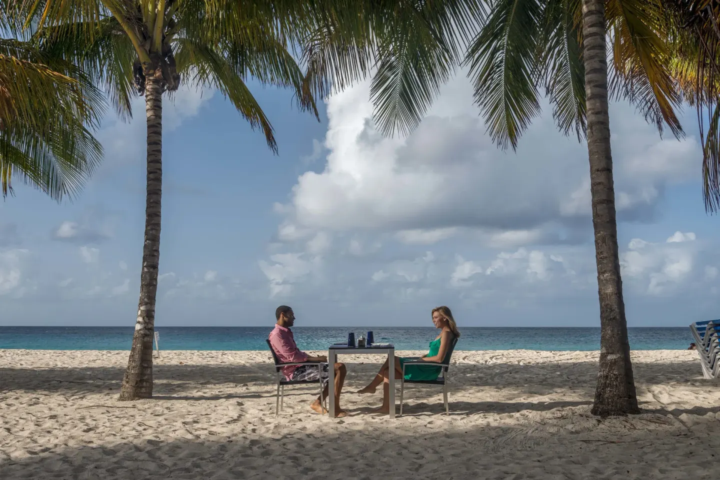Couple seated at a table on the beach under palms at Divi Southwinds Beach Resort.