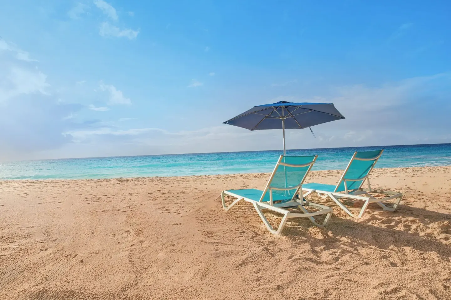 Two turquoise beach loungers and an umbrella face the ocean at Divi Southwinds Beach Resort.