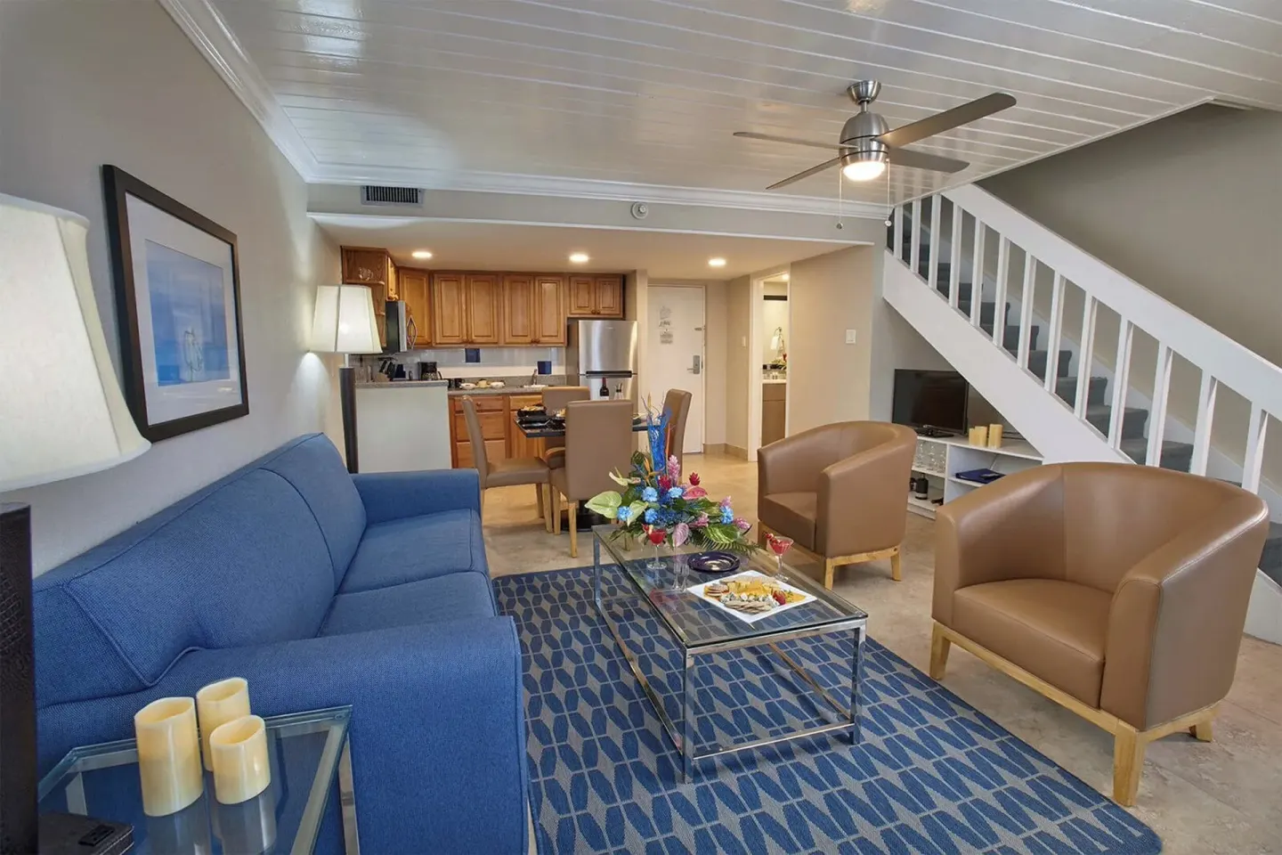 Living area with blue sofa, armchairs, kitchen, and staircase at Divi Southwinds Beach Resort.