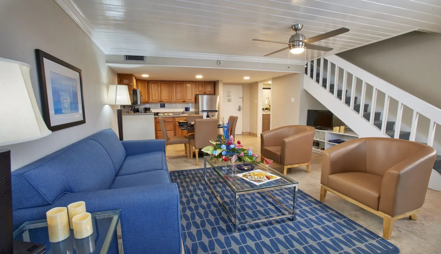 Suite living room with sofa, armchairs, kitchen, and stairs at Divi Southwinds Beach Resort.