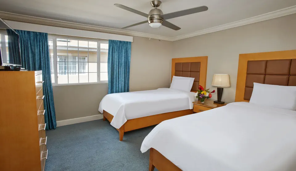 Two-bed bedroom with blue curtains in a two-bedroom suite at Divi Southwinds Beach Resort.