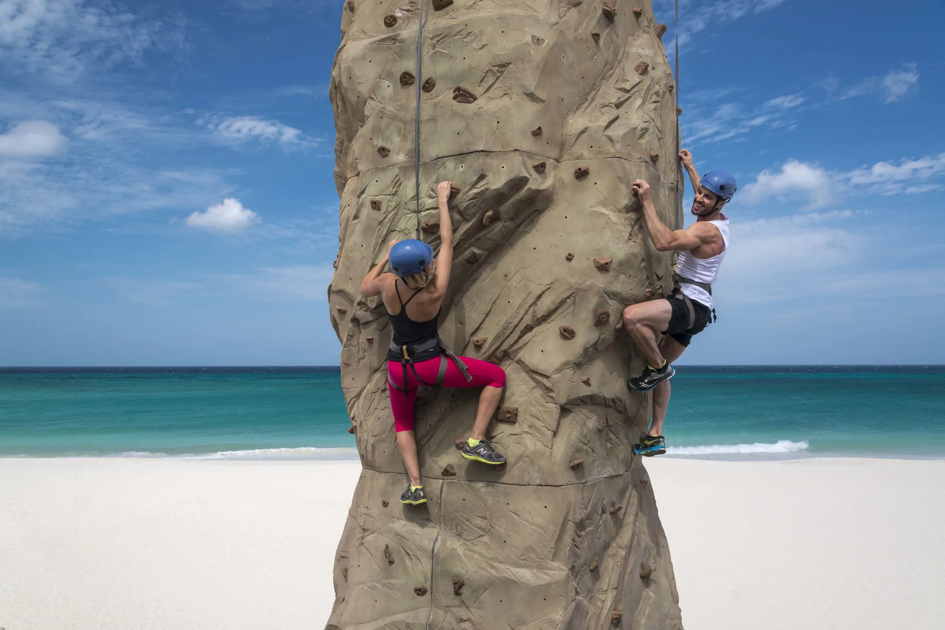 Guests climb an outdoor rock wall by the beach at Divi Village Golf & Beach Resort.