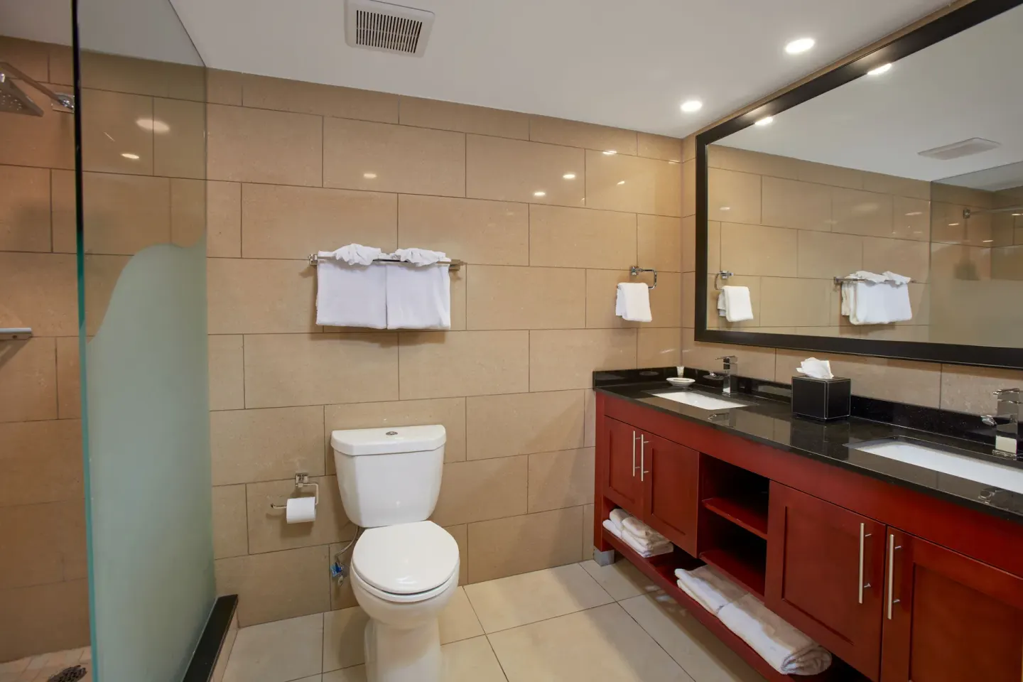 Guest bathroom with toilet, double vanity, and glass shower at Divi Village Golf & Beach Resort.