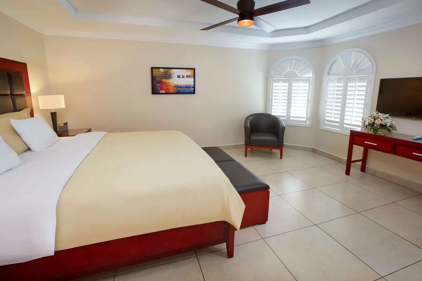 King bed with arched shuttered windows and TV at Divi Village Golf & Beach Resort.