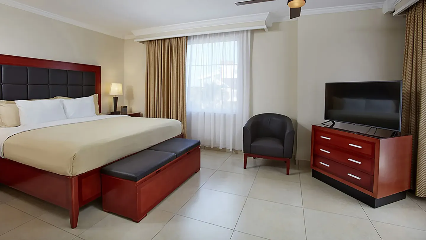King bed, chair and TV beside a curtained window at Divi Village Golf & Beach Resort.