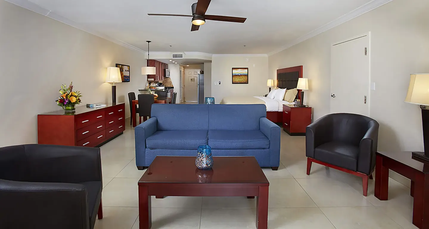 Open suite with blue sofa, chairs, bed and kitchen at Divi Village Golf & Beach Resort.