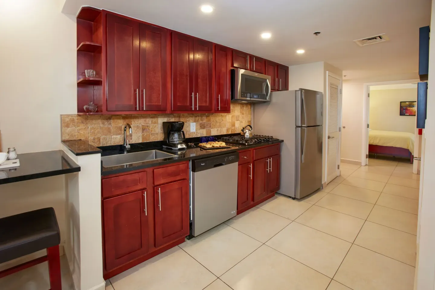 Suite kitchen at Divi Village Golf & Beach Resort with red cabinets, refrigerator, and bedroom doorway.