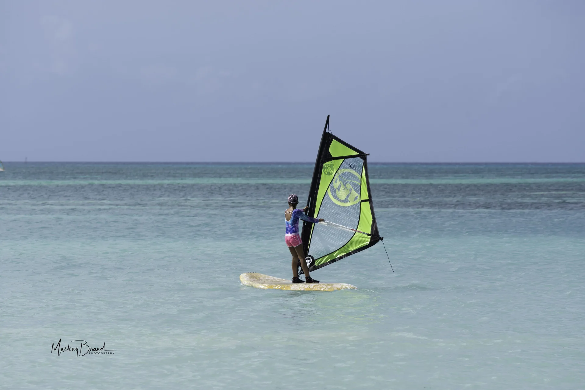 A windsurfer sails across shallow turquoise water at Divi Village Golf & Beach Resort.