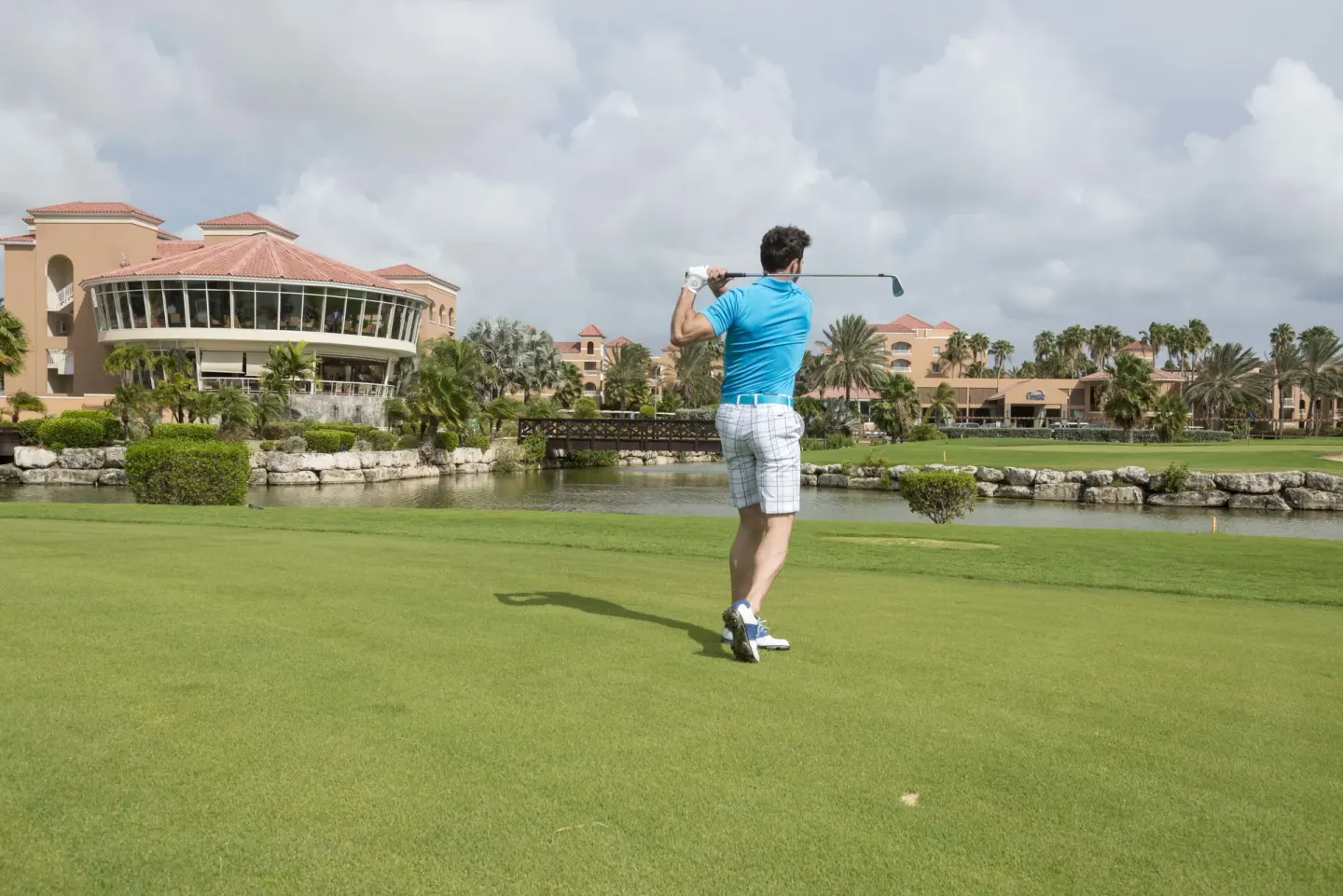 A golfer swings on a fairway facing resort buildings at Divi Village Villas.