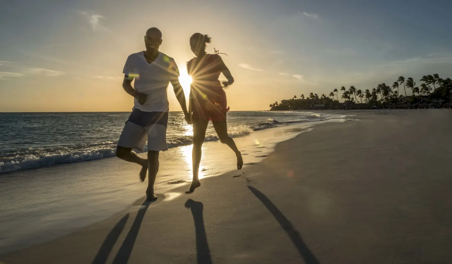 Couple running along the shoreline at sunset near Divi Village Villas.