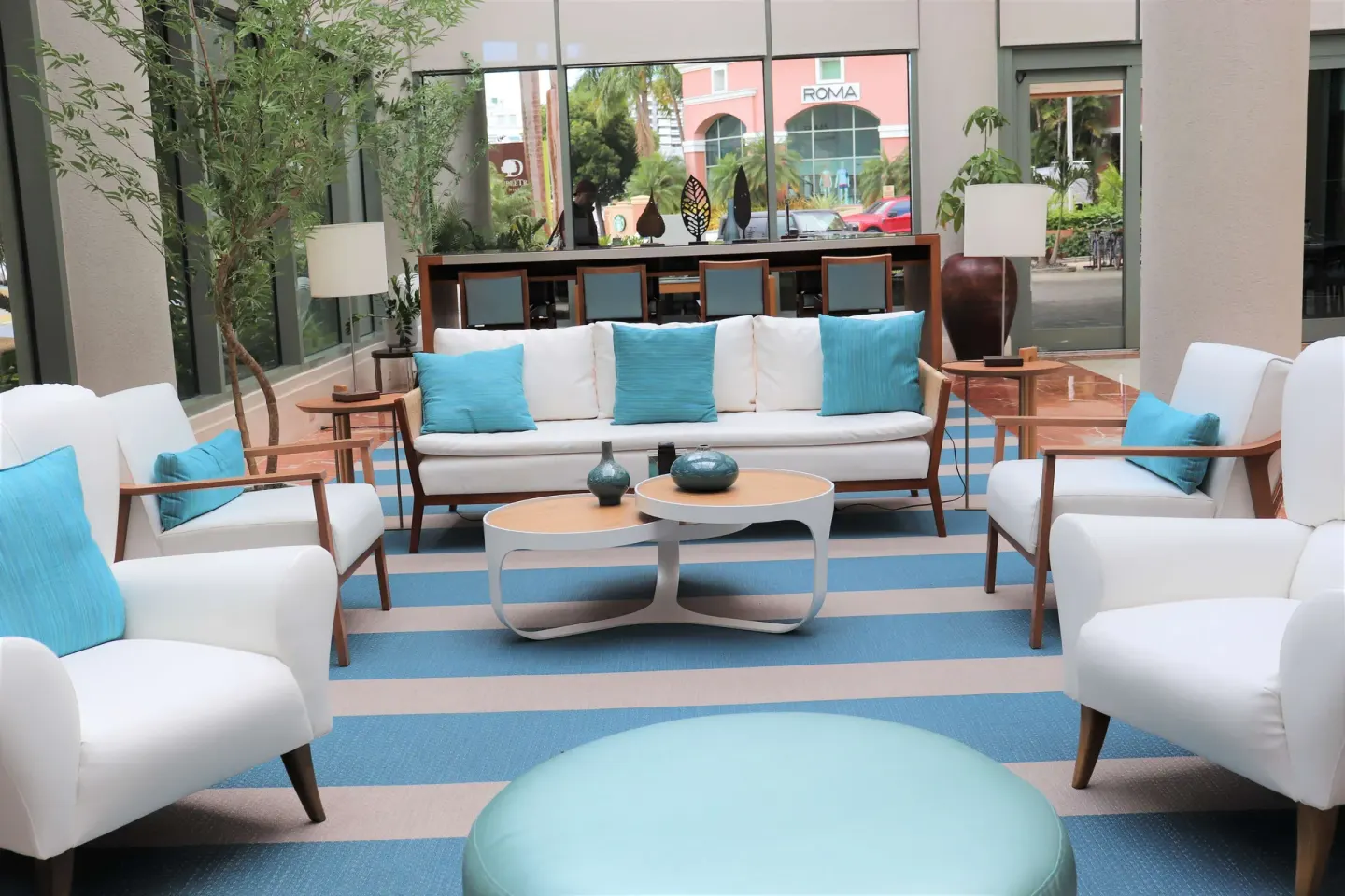 Lobby seating with white chairs, turquoise pillows, and street-facing windows at DoubleTree San Juan.