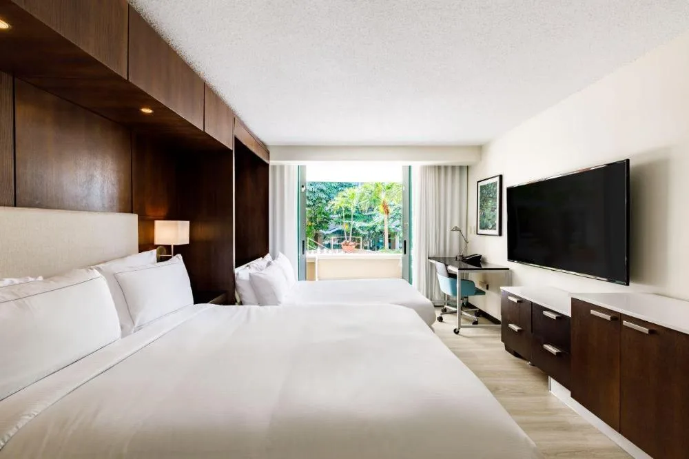 Two white beds, wall-mounted TV, desk, and balcony window in a room at DoubleTree San Juan.