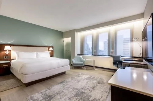 Corner Room at DoubleTree San Juan with king bed, windows, lounge chair, desk and wall-mounted TV.