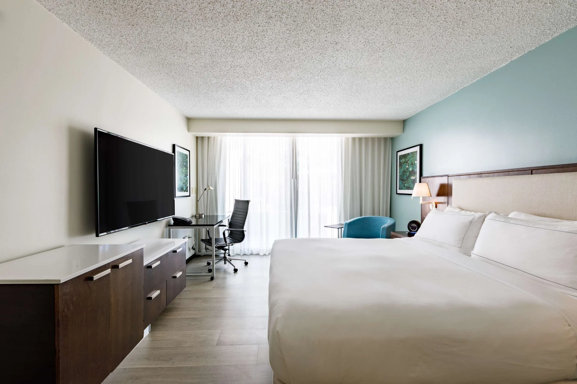 Deluxe guest room with one bed, TV console, desk, and curtained balcony doors at DoubleTree San Juan.