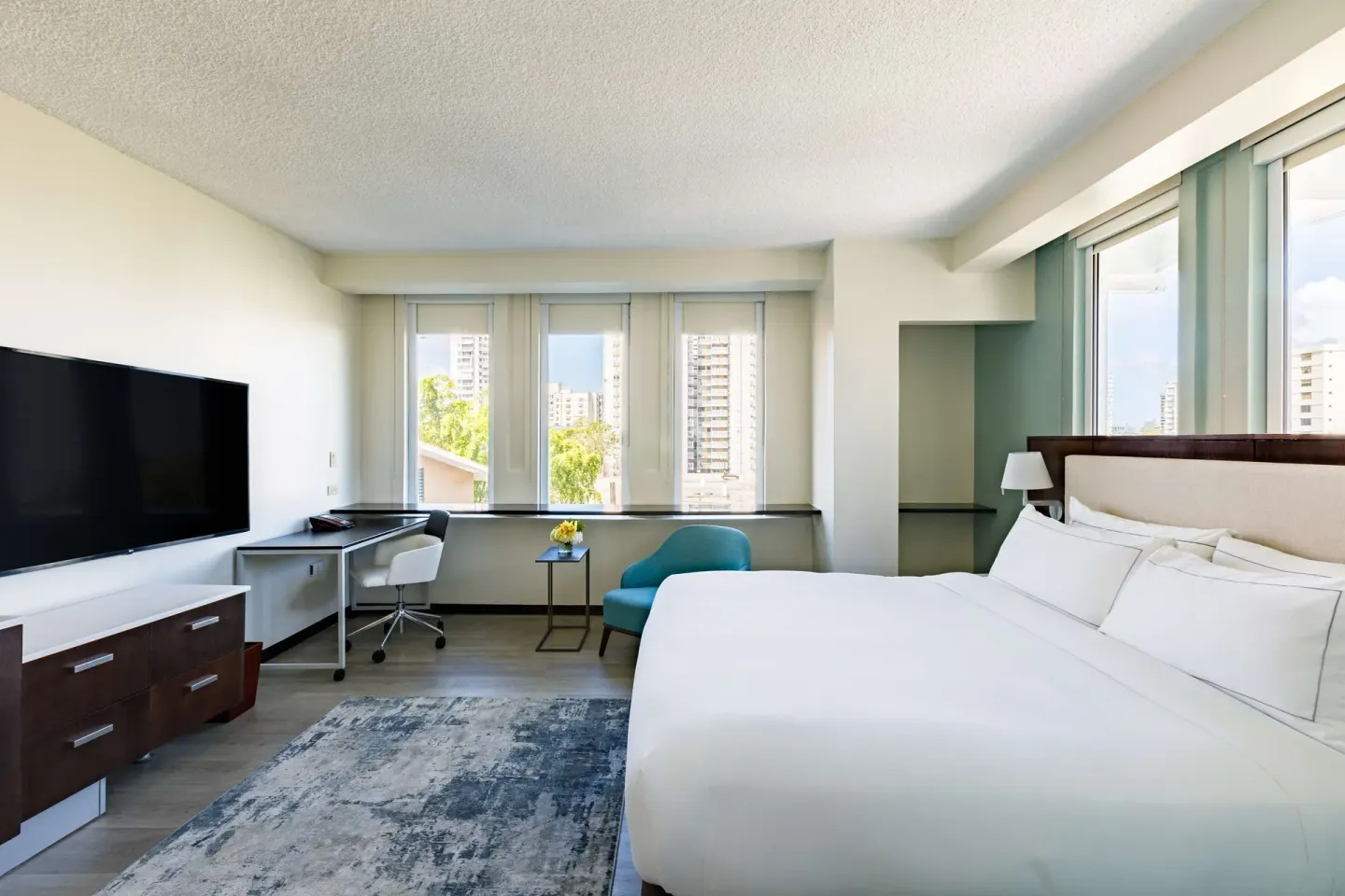 Corner guest room with king bed, TV, desk, and city-facing windows at DoubleTree San Juan.
