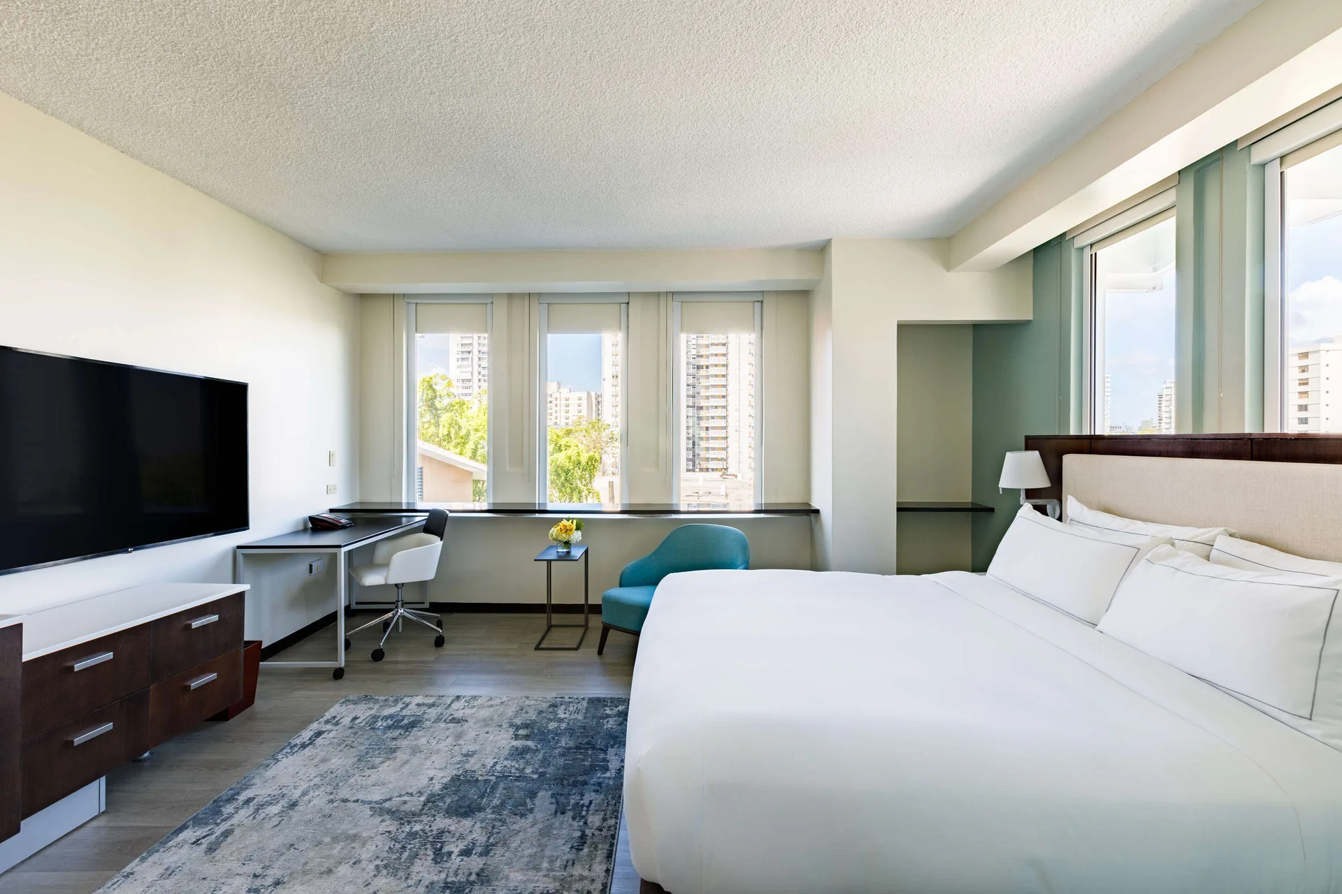 Corner guest room with king bed, TV, desk, and city-facing windows at DoubleTree San Juan.