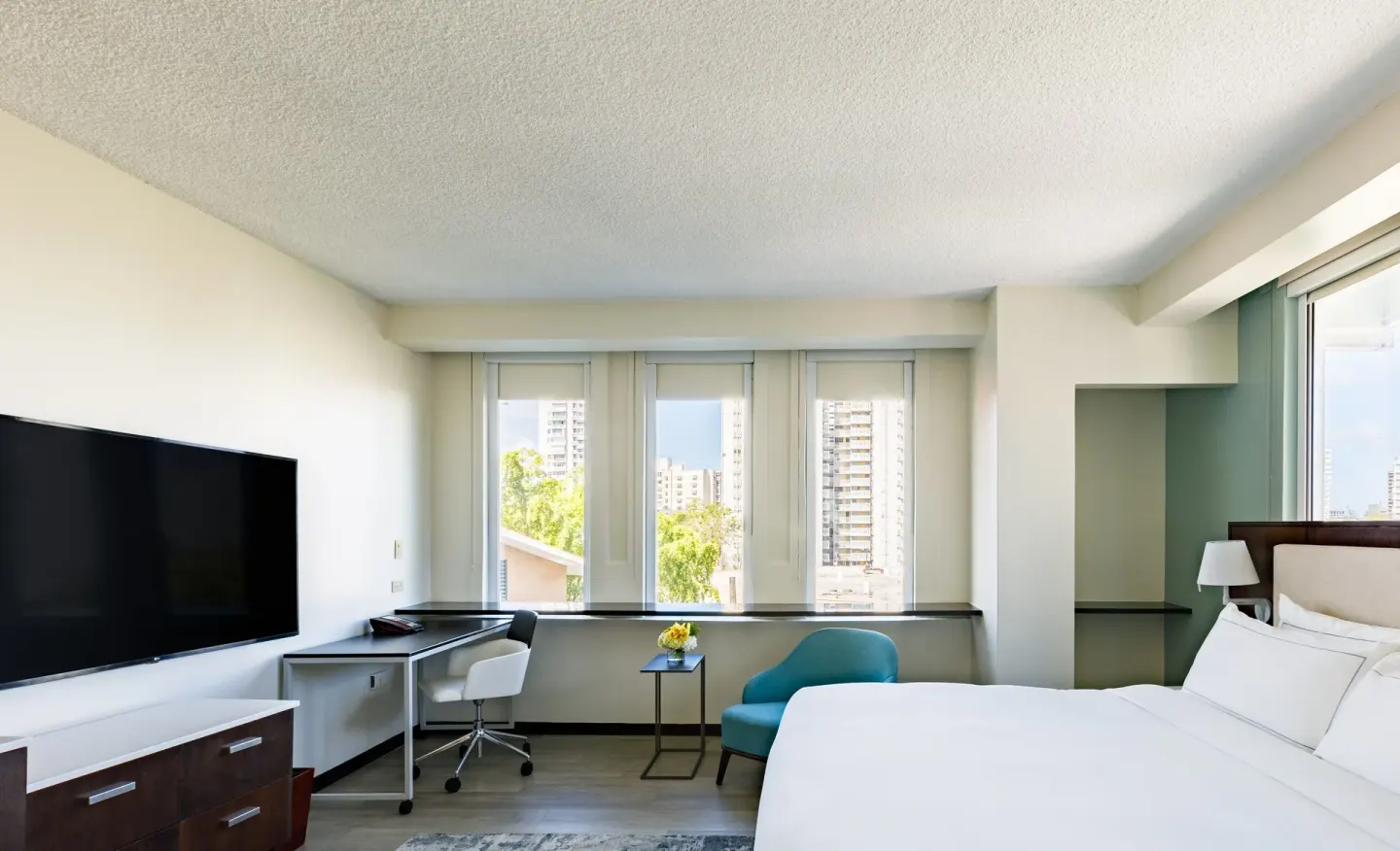 Corner guest room with king bed, TV, work desk, teal chair, and tall windows at DoubleTree San Juan.