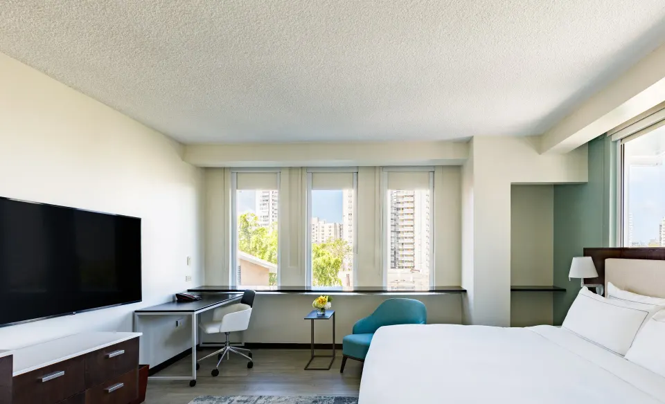 Corner guest room with king bed, TV, work desk, teal chair, and tall windows at DoubleTree San Juan.