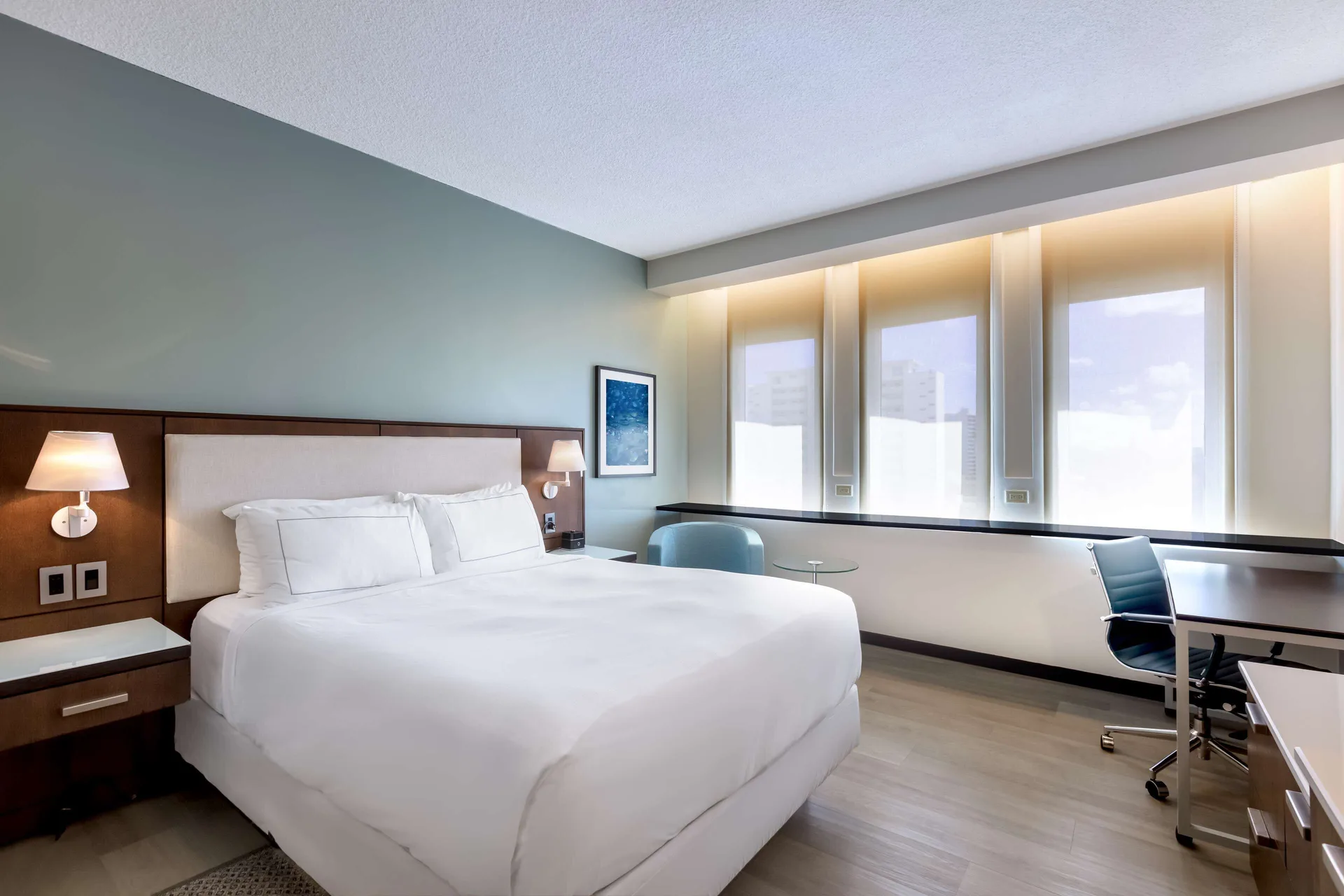 Standard Room at DoubleTree San Juan with a king bed, bedside lamps, desk, and three tall windows.