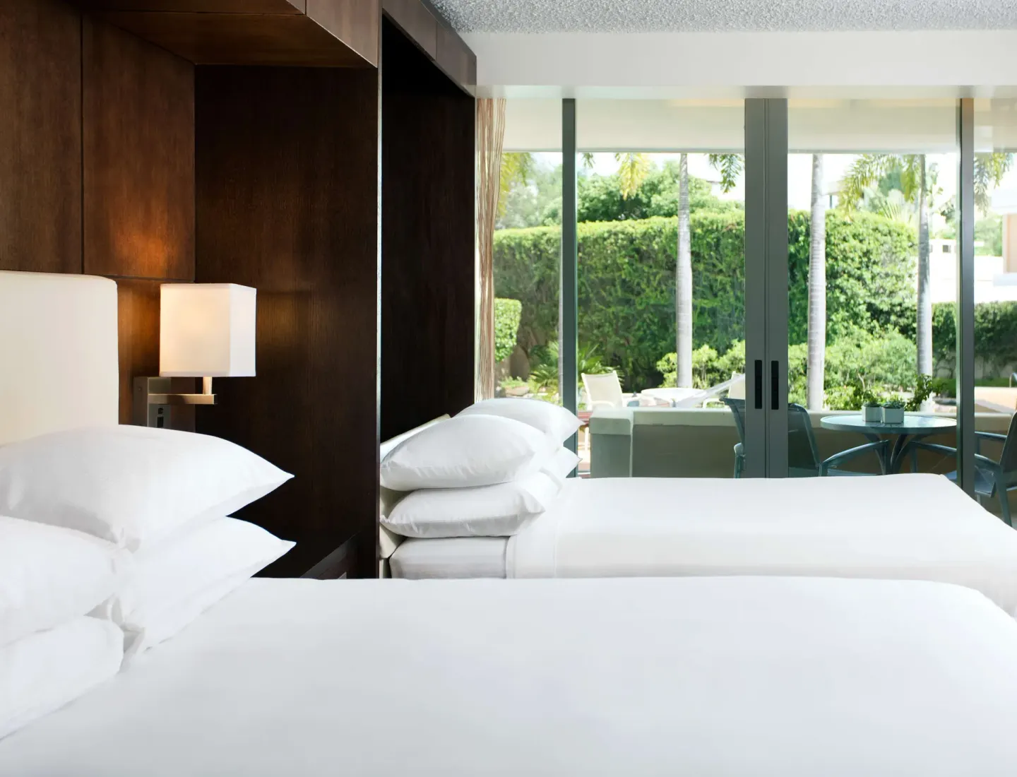 Two white beds in a Standard Room at DoubleTree San Juan with glass doors opening to greenery.