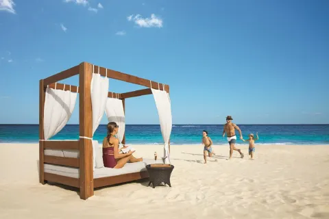 A beach daybed and family playing on the sand at Dreams Riviera Cancun Resort & Spa.