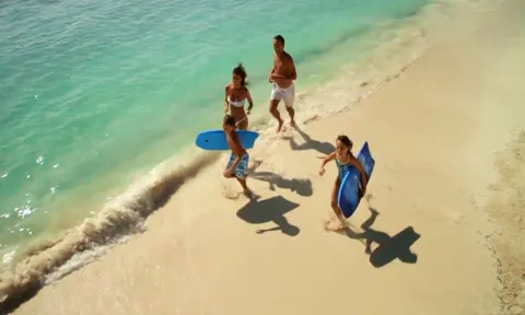 A family runs along the shoreline with bodyboards at Dreams Riviera Cancun Resort & Spa.