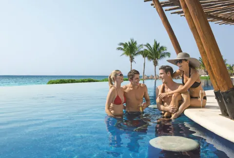 Guests gathered in an infinity pool by the sea at Dreams Riviera Cancun Resort & Spa.