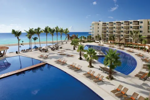 Curved pools and palm-lined deck at Dreams Riviera Cancun Resort & Spa overlooking the beach.